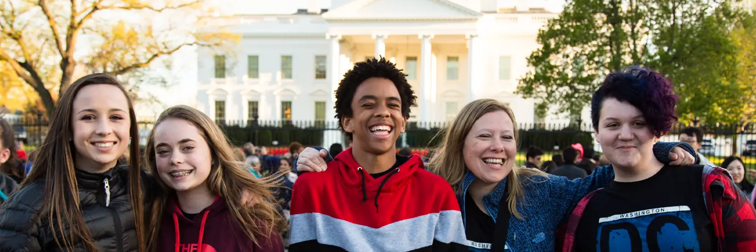 Five students posing for a photo in front of a fence with the White House in the background.